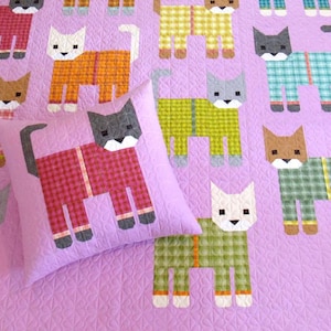 May include: A quilted blanket and pillow set featuring a repeating pattern of geometric cat figures in various colors. The cats are dressed in plaid and solid colors against a light purple background. The pillow is square and features a single cat design.