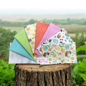 May include: A fan of colorful fabric swatches, including patterns with cats, dots, and textures. The fabrics are arranged on a tree stump, with a label that reads "Something to Sew."