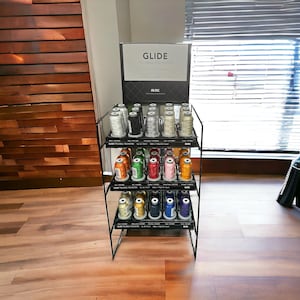 May include: A three-tier metal stand displaying spools of Glide Trilobal Polyester thread in various colors. The stand is labeled "Glide Trilobal Polyester" and "Fil-Tec".