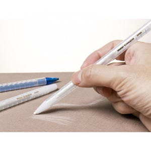 May include: A close-up of a clear, plastic, water-erasable pencil with the text "Water Erasable 3mm" printed on the side. The pencil is being held by a hand and is drawing on a light brown surface.