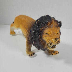 May include: A plastic toy lion figurine with a brown body and a black mane. The lion is in a crouching position with its mouth open, showing its teeth.