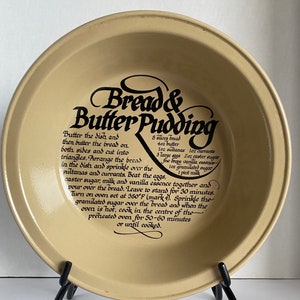 May include: A beige ceramic pie dish with a black and white graphic that reads "Bread & Butter Pudding". The dish includes a recipe for the pudding, listing ingredients such as bread, butter, eggs, sugar, milk, and vanilla essence.