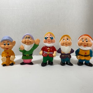 May include: Set of seven plastic figurines of the seven dwarfs from the Disney film Snow White and the Seven Dwarfs. The dwarfs are all wearing different coloured clothing and have different facial expressions.