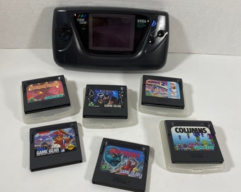 May include: A black Sega Game Gear handheld video game console with six game cartridges. The cartridges include:  "Revenge of the  Dragon", "Batman", "Sonic the Hedgehog 2", "Columns", "Super Monaco GP", and "Namco's  Baseball Stars 2".