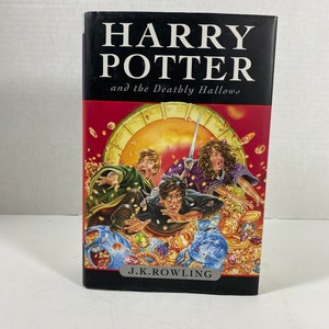 May include: A black hardback book with the title "Harry Potter and the Deathly Hallows" by J.K. Rowling. The cover features an illustration of Harry Potter, Ron Weasley, and Hermione Granger surrounded by gold coins and other treasures.