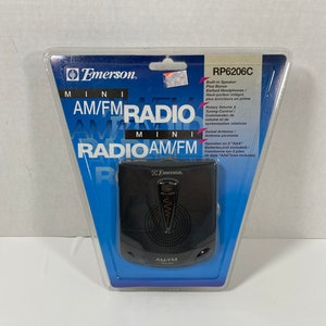 May include: A black Emerson mini AM/FM radio with a swivel antenna, rotary volume and tuning controls, and a built-in speaker. The radio is packaged in a clear plastic blister pack with blue and white packaging. The packaging includes the model number RP6206C.
