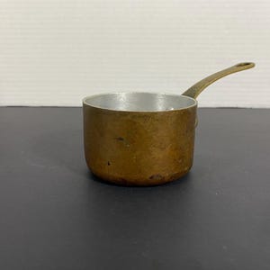 以下が含まれることがあります： 長い取っ手のある小さな銅製の鍋。鍋の内側は銀色で、少し曇っている