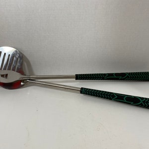 May include: A set of two silver grilling tools with black and green handles. The tools are shaped like golf clubs.