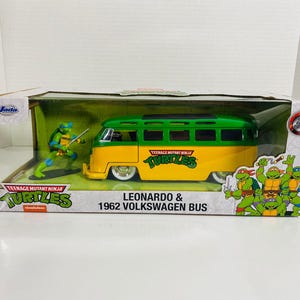 Könnte beinhalten: Modell eines Leonardo & 1962 Volkswagen Bus der Teenage Mutant Ninja Turtles in einer Box. Der Bus ist gelb und grün mit dem Turtles-Logo. Eine Leonardo-Figur ist enthalten. Die Box hat das Teenage Mutant Ninja Turtles-Logo.