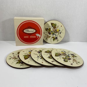 May include: Set of six round, white, acrylic coasters with a brown border. Each coaster features a colourful illustration of birds and berries on a white background. The coasters come in a red and white box with the text "Pimpernel Acrylic Coasters Set of Six Bird & Berry Motif" printed on the front.