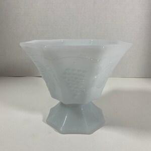 May include: A white milk glass bowl with a grape design. The bowl has a pedestal base and is octagonal in shape.
