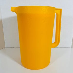 May include: A vibrant yellow pitcher with a handle and a spout. The pitcher is made of textured plastic. It is designed for holding and pouring liquids. The handle is rectangular and attached to the side of the pitcher. It is approximately 25 cm tall.