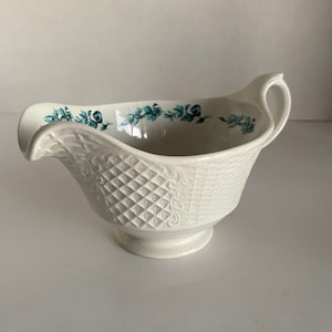 May include: White ceramic gravy boat with a blue floral design around the rim and a raised, textured pattern on the body.
