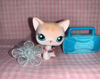 Pode incluir: Um brinquedo de gato branco e laranja com olhos azuis e um colar de contas coloridas. O gato está sentado ao lado de um toca-fitas azul.