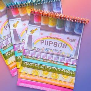 Könnte beinhalten: Spiralgebundene Notizbücher mit farbenfrohen Washi-Tape-Designs. Die Notizbücher zeigen ein hawaiianisches Nummernschild-Design mit dem Text "PUP808 ALOHA STATE". Die Oberseite der Notizbücher hat farbenfrohe Spiralbindungen.