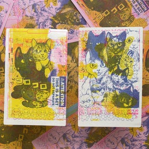 May include: Two illustrated cards with a colorful design featuring cats. The cards have a pink and yellow background with black and white text that reads "ATTENTION THIS IS A SET DO NOT SEPARATE".