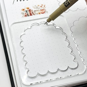 May include: A clear acrylic stencil with a scalloped edge, used for drawing or writing in a planner or journal.