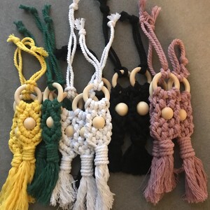May include: Six macrame keychains with wooden beads and rings. The keychains are in yellow, green, white, black, and pink.