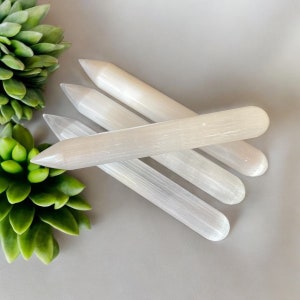 May include: Four white selenite wands with pointed ends. The wands are smooth and polished, with a slightly translucent appearance.