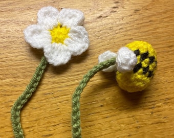 May include: A crocheted bookmark with a white daisy flower and a yellow and black bee. The stem is green.
