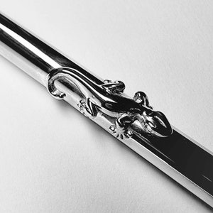 May include: A silver pen with a detailed lizard design on the barrel.
