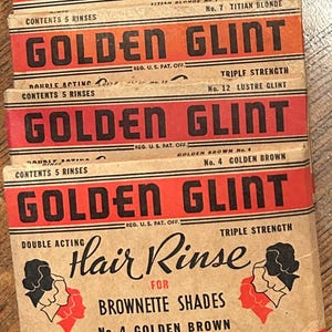 May include: Vintage Golden Glint hair rinse boxes. The boxes are red and tan with bold black text. The boxes are labeled with the Golden Glint brand name, product information, and the phrase "Tints Your Hair As It Rinses."