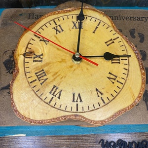 May include: A wooden clock with Roman numeral markings on a natural wood slice. The clock hands are black and red.