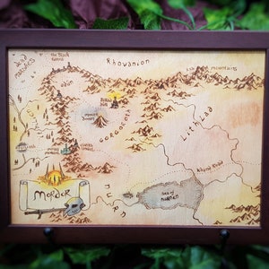May include: A hand-painted wooden map of Middle-earth, featuring the land of Mordor, the Black Gate, and the Sea of Nurnen. The map is framed in a dark brown wood frame.