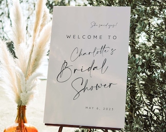 May include: White welcome sign with black calligraphy text that reads "She said yes! Welcome to Charlotte's Bridal Shower May 6, 2023".