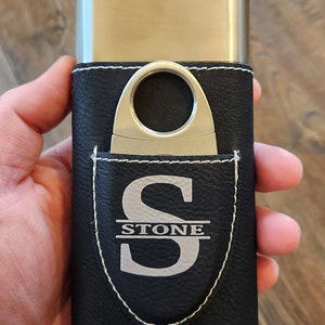 May include: A black leather cigar case with a silver metal cigar cutter and a silver monogram that reads "STONE".