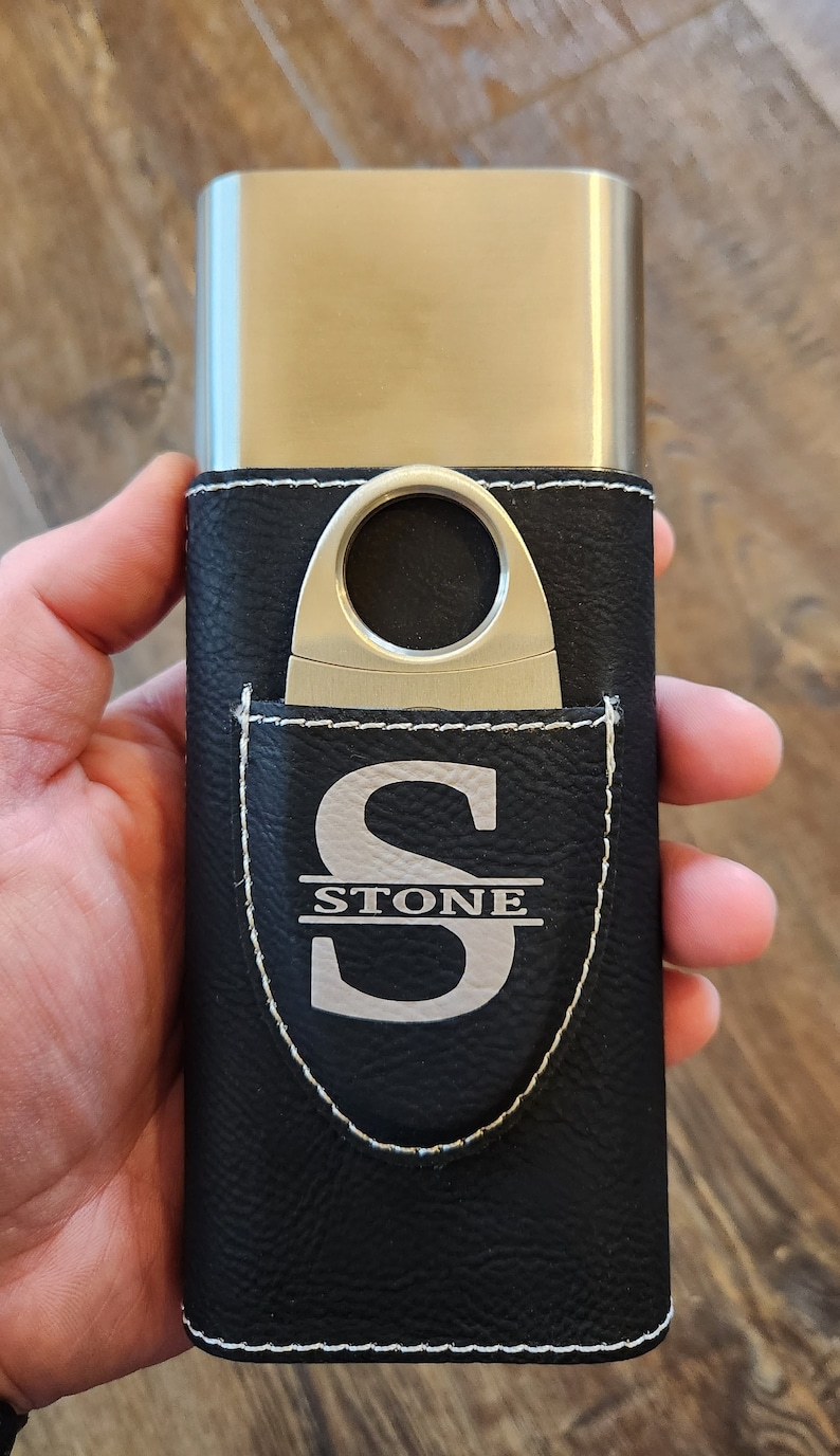 May include: A black leather cigar case with a silver metal cigar cutter and a silver monogram that reads "STONE".