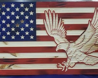 Può includere: Una bandiera americana in legno con una finitura rossa, bianca e blu invecchiata. Un'aquila bianca è scolpita nel legno, che vola sopra la bandiera.