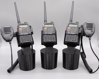 May include: Three black two-way radios with antennas and microphones are displayed on a black stand. The radios have a keypad and a small screen.
