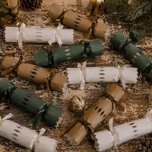 May include: A collection of cylindrical Christmas crackers in white, forest green, and kraft brown paper. Each cracker features a central diamond-cut pattern, scalloped edges, and is tied at both ends with matching satin ribbons.