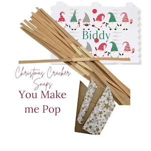 K&ouml;nnte beinhalten: Ein Set Weihnachtscracker-Schnipser mit einem Gnom-Motiv. Das Set enth&auml;lt braune Papierstreifen, goldstern gemustertes Papier und eine wei&szlig;e Karte mit einem Gnom-Design und dem Text "Biddy". Der Text "Christmas Cracker Snaps You Make me Pop" ist auf die Karte gedruckt.