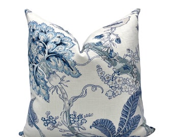 May include: A square throw pillow featuring a white fabric base with a blue botanical print. The pattern displays large stylized flowers, leafy branches, and small floral clusters in varying shades of blue, creating a detailed and intricate design.