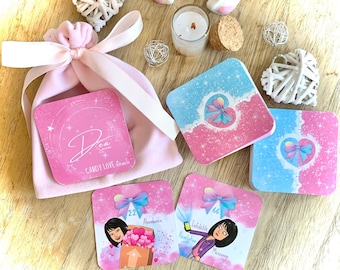 May include: A pink satin bag with a white ribbon and a pink card with the text "Dea & Sia CANDY LOVE Oracle" on it. There are three pink and blue oracle cards with illustrations of women and text. The cards are on a wooden surface.