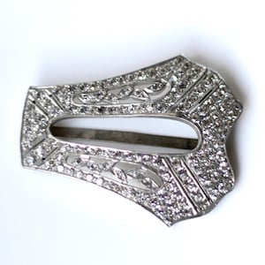 May include: A silver-toned metal belt buckle with a decorative design of small rhinestones set in a geometric pattern.