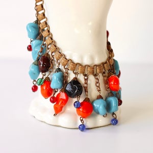 Puede incluir: Un collar de cadena dorada con una franja de cuentas de vidrio de colores. Las cuentas son en tonos de azul, rojo, naranja, verde y marrón.
