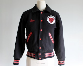 Op de afbeelding: Zwarte vintage letterman-jas met rode accenten. Voorzien van een "Boyertown" patch met een berenlogo en de naam "Dave" in het rood geborduurd. De jas heeft rood-wit gestreepte manchetten en tailleband.