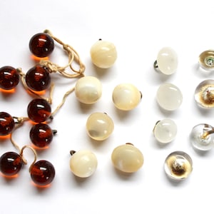 May include: Assortment of vintage buttons in various colors and materials, including brown glass, white and cream-colored plastic, and clear glass with gold accents.