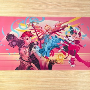 A pink mouse pad featuring three video game characters. The center character is glowing with light and holding a staff. The character on the right is striking a pose with a weapon. The character on the left is holding a glowing orb.