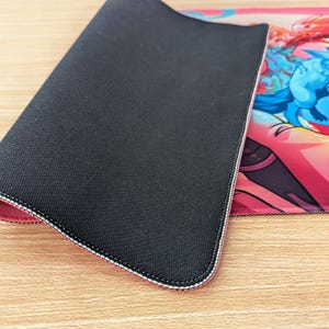 The mouse pad is folded in half so you can see the bottom and top of it. The bottom is black rubber and has a grippy texture. There’s stitching around the edges on the front and back.