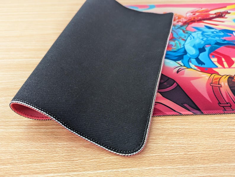 The mouse pad is folded in half so you can see the bottom and top of it. The bottom is black rubber and has a grippy texture. There’s stitching around the edges on the front and back.