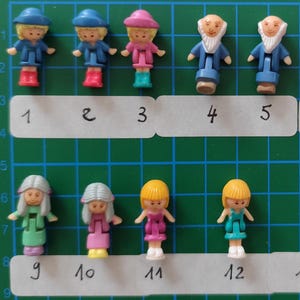 Può includere: Una collezione di 15 piccole figurine di plastica, tra cui ragazze e uomini con la barba, che indossano abiti diversi. Le figurine sono disposte in due file su una superficie verde a griglia.