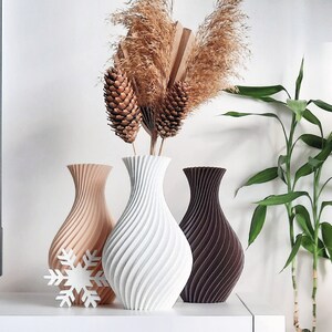 Pu&ograve; includere: Tre vasi in ceramica di diversi colori e design. Il vaso a sinistra &egrave; beige con un motivo a spirale, il vaso al centro &egrave; bianco con un motivo a spirale e il vaso a destra &egrave; marrone con un motivo a spirale. I vasi sono disposti su una superficie bianca con fiori secchi sullo sfondo.