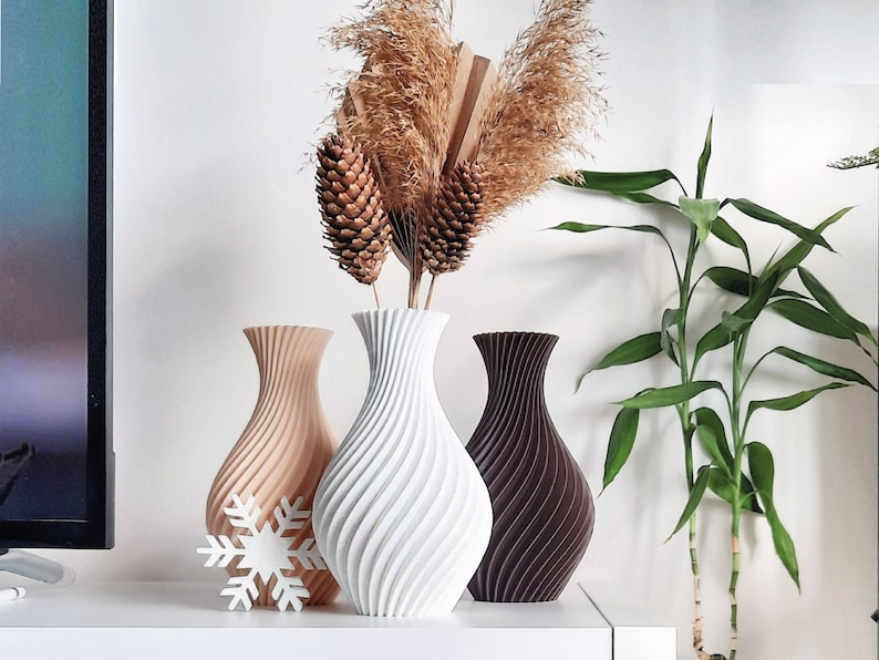 Pu&ograve; includere: Tre vasi in ceramica di diversi colori e design. Il vaso a sinistra &egrave; beige con un motivo a spirale, il vaso al centro &egrave; bianco con un motivo a spirale e il vaso a destra &egrave; marrone con un motivo a spirale. I vasi sono disposti su una superficie bianca con fiori secchi sullo sfondo.