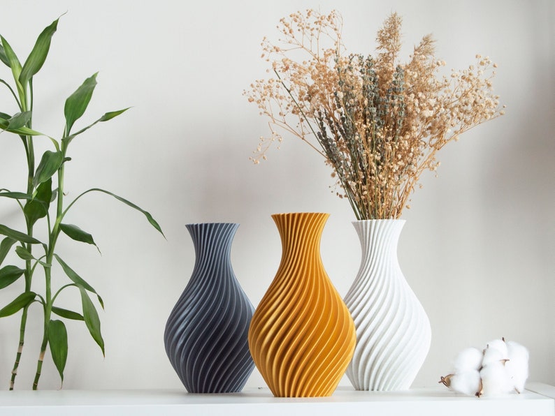 Pu&ograve; includere: Tre vasi decorativi con un motivo a spirale. I vasi sono grigi, gialli e bianchi. Il vaso giallo &egrave; pieno di fiori secchi.