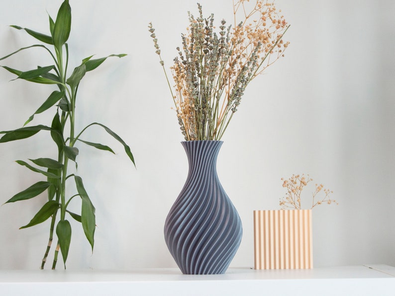 Pu&ograve; includere: Due vasi con fiori secchi. Il vaso pi&ugrave; grande &egrave; grigio e ha un motivo a spirale. Il vaso pi&ugrave; piccolo &egrave; arancione chiaro e ha un motivo a righe.