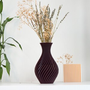 Pu&ograve; includere: Due vasi con fiori secchi. Il vaso pi&ugrave; grande &egrave; di colore viola scuro con un motivo a spirale. Il vaso pi&ugrave; piccolo &egrave; di colore arancione chiaro con un motivo a coste verticali.